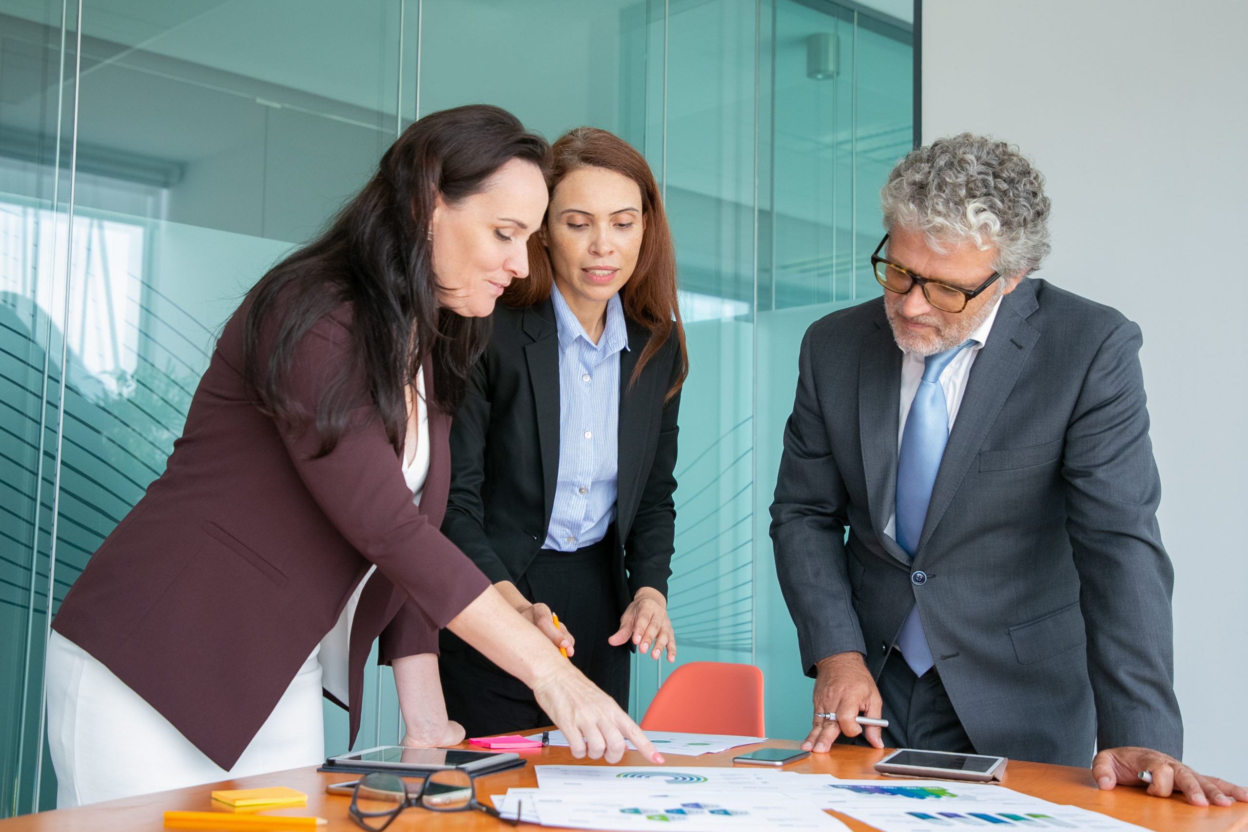 Group of professionals analyzing paper reports with charts and graphs. Business team standing at table, looking and pointing at marketing documents and talking. Analysis and teamwork concept